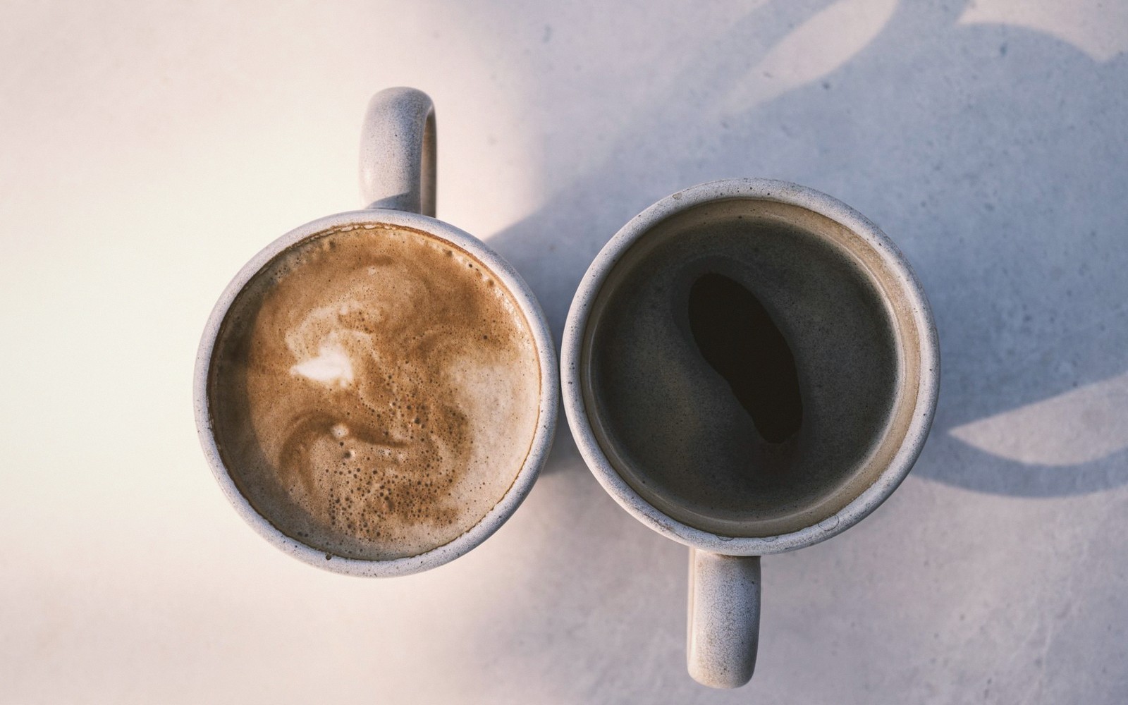 Two mugs viewed from above, one with milky foam and one with black coffee